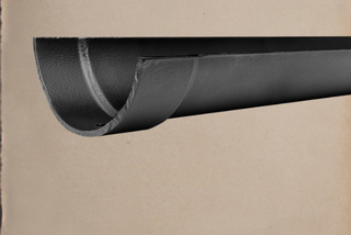 A close-up of a dark charcoal gray leather curtain rod with a textured finish, shown against a warm beige background with the 'TRADCAST by Guttercrest' logo in the top right corner.